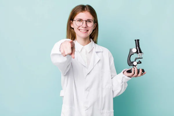 red head pretty woman pointing at camera choosing you. scientist with microscope concept