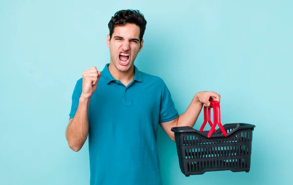 怒りの表情で積極的に叫んでいるハンサムなヒスパニック系の男 ショッピングバスケットのコンセプト — ストック写真