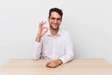 İspanyol yakışıklı adam kendini mutlu hissediyor, iyi bir jestle onaylıyor. iş adamı ve masa başı konsepti