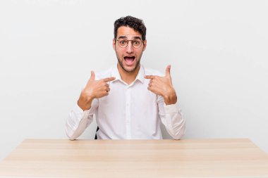 İspanyol yakışıklı adam mutlu hissediyor ve heyecanla kendini işaret ediyor. iş adamı ve masa başı konsepti