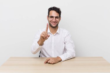 Hispanik yakışıklı adam gururla gülümsüyor ve kendinden emin bir numara oluyor. iş adamı ve masa başı konsepti