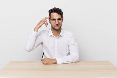 İspanyol yakışıklı adam kafası karışık ve şaşkın hissediyor, senin deli olduğunu gösteriyor. iş adamı ve masa başı konsepti