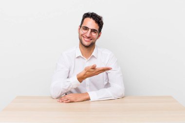 İspanyol yakışıklı adam neşeyle gülümsüyor, mutlu hissediyor ve bir konsept gösteriyor. iş adamı ve masa başı konsepti