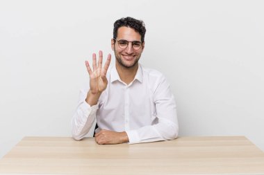 İspanyol yakışıklı adam gülümsüyor ve arkadaş canlısı görünüyor, dört numarayı gösteriyor. iş adamı ve masa başı konsepti