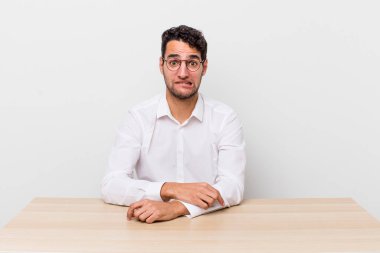 İspanyol yakışıklı adam kafası karışmış ve şaşkın görünüyor. iş adamı ve masa başı konsepti