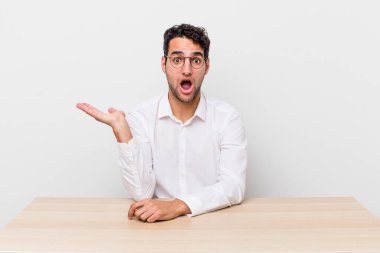İspanyol yakışıklı adam şaşırmış ve şok olmuş görünüyor. Çenesi düşmüş ve elinde bir nesne var. iş adamı ve masa başı konsepti