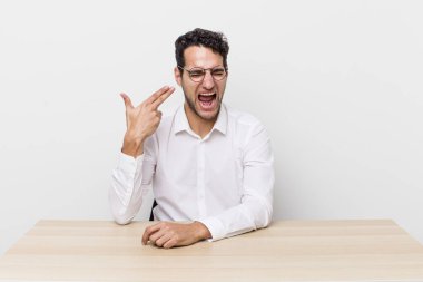 İspanyol yakışıklı adam mutsuz ve stresli görünüyor, intihar jesti silah işareti yapıyor. iş adamı ve masa başı konsepti