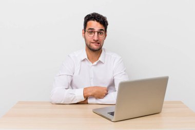 İspanyol yakışıklı adam kafası karışmış ve şaşkın görünüyor. iş adamı ve masa başı konsepti