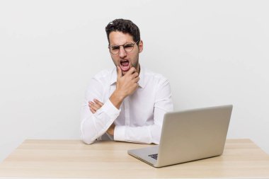 Ağzı ve gözleri açık, eli çenesinde İspanyol yakışıklı bir adam. iş adamı ve masa başı konsepti