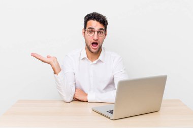 İspanyol yakışıklı adam şaşırmış ve şok olmuş görünüyor. Çenesi düşmüş ve elinde bir nesne var. iş adamı ve masa başı konsepti