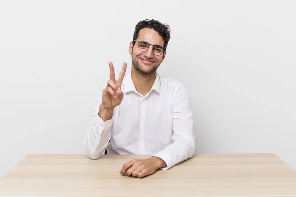 ヒスパニック系のハンサムな男は笑顔と幸せそうに見える勝利や平和をジェスチャー ビジネスマンとデスクのコンセプト — ストック写真