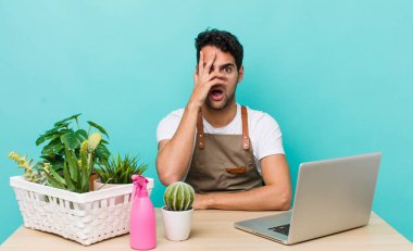 İspanyol yakışıklı adam şok olmuş, korkmuş ya da korkmuş görünüyor. Yüzü elle kapatılmış. bahçe ve bitki konsepti