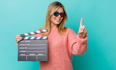 Güzel sarışın kadın gülümsüyor ve arkadaş canlısı görünüyor. Bir numarayı gösteriyor. Sinema kavramı