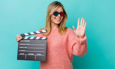 Güzel sarışın kadın gülümsüyor ve arkadaş canlısı görünüyor, beş numarayı gösteriyor. Sinema kavramı