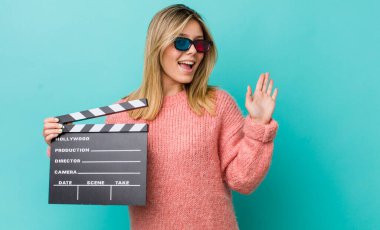 Güzel sarışın kadın mutlu bir şekilde gülümsüyor, el sallıyor, hoş geldin diyor ve seni selamlıyor. Sinema kavramı