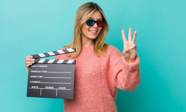 Güzel sarışın kadın gülümsüyor ve arkadaş canlısı görünüyor, üç numarayı gösteriyor. Sinema kavramı