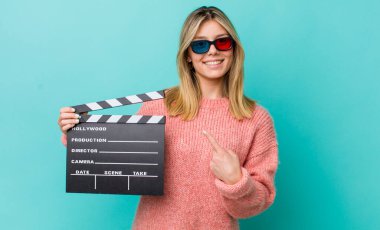 Güzel sarışın kadın neşeyle gülümsüyor, mutlu hissediyor ve bir tarafı işaret ediyor. Sinema kavramı