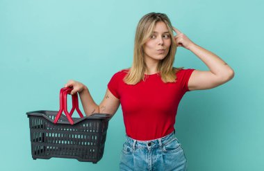 Güzel sarışın kadın mutlu bir şekilde gülümsüyor ve hayal kuruyor ya da şüphe ediyor. Alışveriş sepeti konsepti