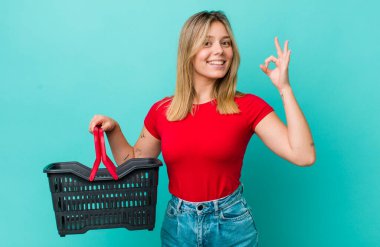 Güzel sarışın kadın kendini mutlu hissediyor, iyi bir jestle onaylıyor. Alışveriş sepeti konsepti