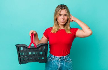 Güzel sarışın kadın şaşkın ve şaşkın hissediyor, deli olduğunu gösteriyor. Alışveriş sepeti konsepti