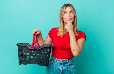 Güzel sarışın kadın düşünüyor, kuşkulu ve şaşkın hissediyor. Alışveriş sepeti konsepti