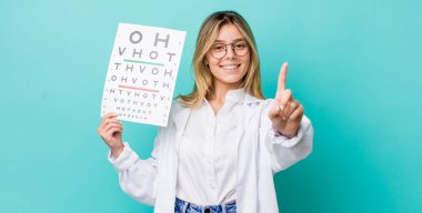 Güzel sarışın kadın gülümsüyor ve arkadaş canlısı görünüyor. Bir numarayı gösteriyor. optik görüş testi konsepti