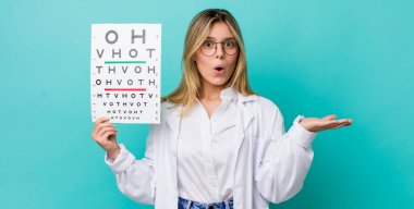 Güzel sarışın kadın şaşırmış ve şok olmuş görünüyor. Çenesi düşmüş ve elinde bir nesne var. optik görüş testi konsepti