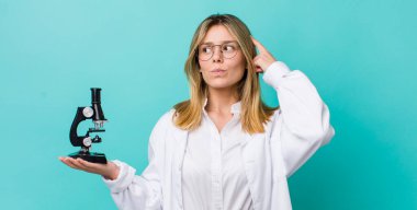 Güzel sarışın kadın şaşkın ve kafası karışık, kaşınıyor. Bilim adamı ve mikroskop kavramı