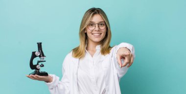 Güzel sarışın kadın seni seçen kamerayı işaret ediyor. Bilim adamı ve mikroskop kavramı