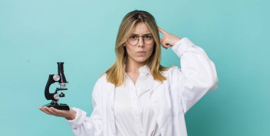 Güzel sarışın kadın şaşkın ve şaşkın hissediyor, deli olduğunu gösteriyor. Bilim adamı ve mikroskop kavramı