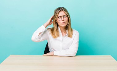 Güzel sarışın kadın mutlu bir şekilde gülümsüyor ve hayal kuruyor ya da şüphe ediyor. iş ve masa konsepti