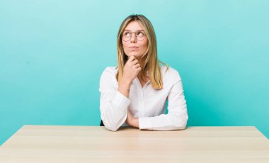 Güzel sarışın kadın düşünüyor, kuşkulu ve şaşkın hissediyor. iş ve masa konsepti