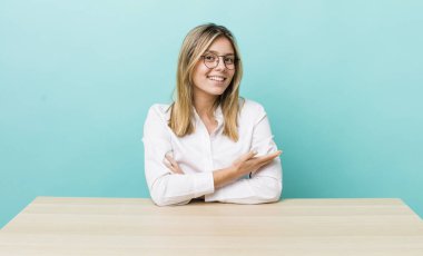 Güzel sarışın kadın neşeyle gülümsüyor, mutlu hissediyor ve bir konsept gösteriyor. iş ve masa konsepti