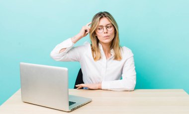 Güzel sarışın kadın şaşkın ve kafası karışık, kaşınıyor. iş ve masa konsepti