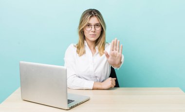 Güzel sarışın kadın ciddi görünüyor. Avuç içi gösteriyor. Durma hareketi yapıyor. iş ve masa konsepti