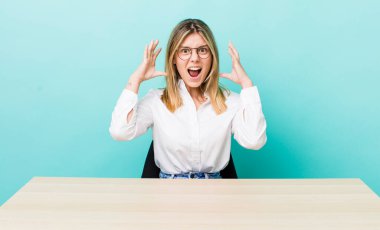 Güzel sarışın kadın ellerini havaya kaldırarak çığlık atıyor. iş ve masa konsepti