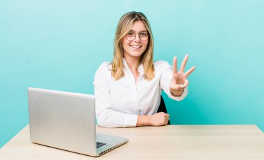 Güzel sarışın kadın gülümsüyor ve arkadaş canlısı görünüyor, üç numarayı gösteriyor. iş ve masa konsepti