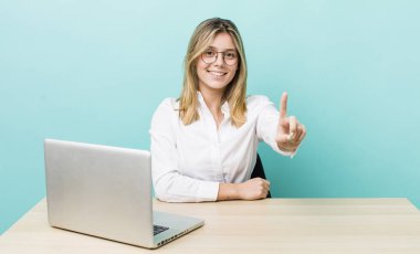 Güzel sarışın kadın gülümsüyor ve arkadaş canlısı görünüyor. Bir numarayı gösteriyor. iş ve masa konsepti