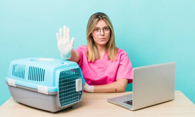 Güzel sarışın kadın ciddi görünüyor. Avuç içi gösteriyor. Durma hareketi yapıyor. Veterinerlik kavramı