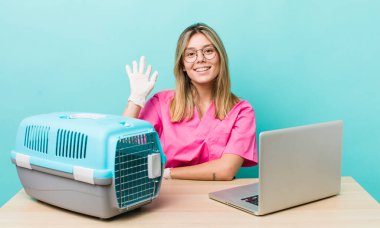 Güzel sarışın kadın mutlu bir şekilde gülümsüyor, el sallıyor, hoş geldin diyor ve seni selamlıyor. Veterinerlik kavramı