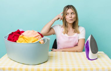 Güzel sarışın kadın şaşkın ve kafası karışık, kaşınıyor. Demir ve giysi konsepti