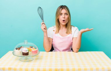 Güzel sarışın kadın şaşırmış ve şok olmuş görünüyor. Çenesi düşmüş ve elinde bir nesne var. Ev yapımı kek konsepti