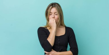 Genç, güzel, sarışın bir kadın ciddi, düşünceli ve endişeli. Eli çenesine değmiş şekilde yan yan bakıyor.