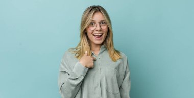 Genç ve güzel sarışın kadın mutlu, gururlu ve şaşırmış görünüyor, neşeli bir şekilde kendini gösteriyor, kendinden emin ve kibirli hissediyor.