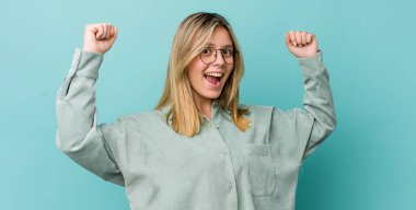 Genç, güzel, sarışın bir kadın muzaffer bir şekilde bağırıyor. Heyecanlı, mutlu ve şaşırmış görünüyor.