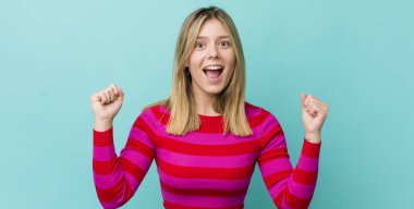 Genç, güzel sarışın kadın mutlu, pozitif ve başarılı hissediyor zaferi, başarıları ya da iyi şansı kutluyor.