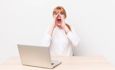 Kızıl saçlı, güzel bir kadın kendini mutlu hissediyordu. Elleri ağzının kenarında bağırıyordu. iş kavramı