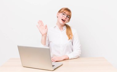 Kızıl saçlı güzel kadın mutlu bir şekilde gülümsüyor, el sallıyor, seni selamlıyor ve selamlıyor. iş kavramı