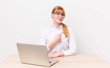 Kızıl saçlı güzel bir kadın neşeyle gülümsüyor, mutlu hissediyor ve bir tarafı işaret ediyor. iş kavramı