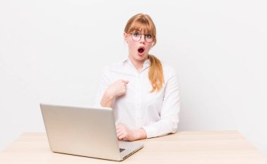 Kızıl saçlı güzel kadın şok olmuş ve ağzı açık, kendini işaret eden bir şekilde şaşırmış görünüyor. iş kavramı